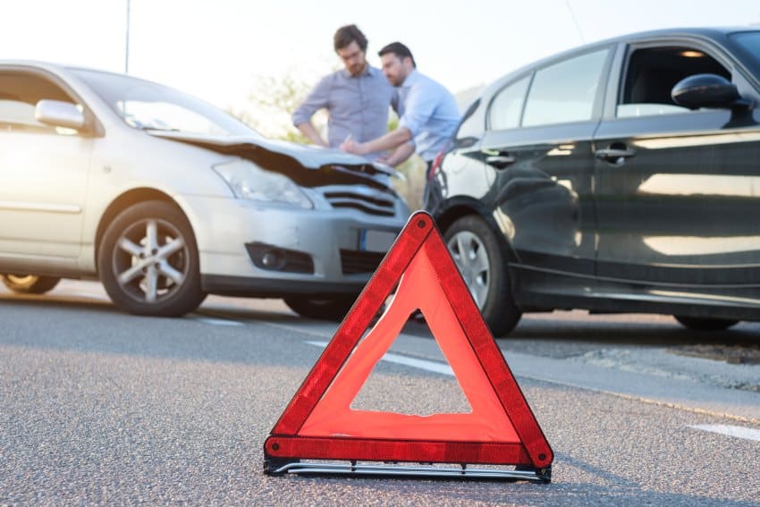 Reflective triangle red hazard sign in front of two men beside silver and black car after a car accident exchanging details