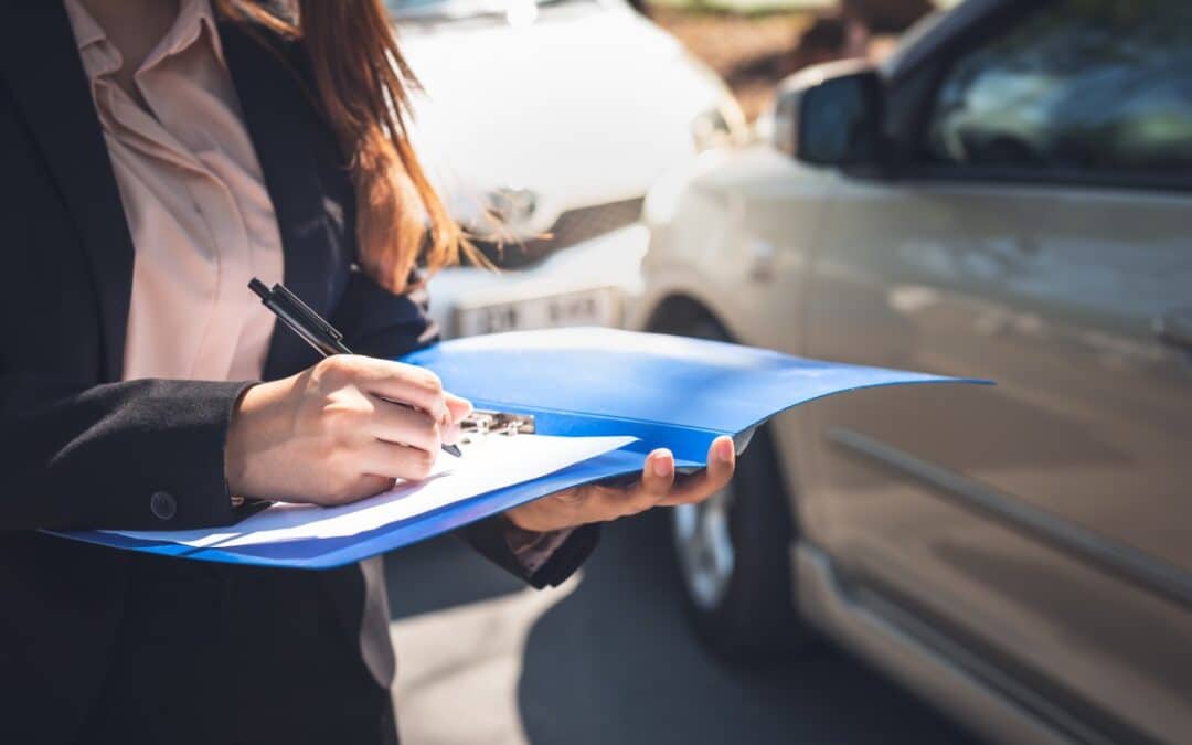 Female insurance agent writing accident report in blue folder after front collision car crash between two vehicles